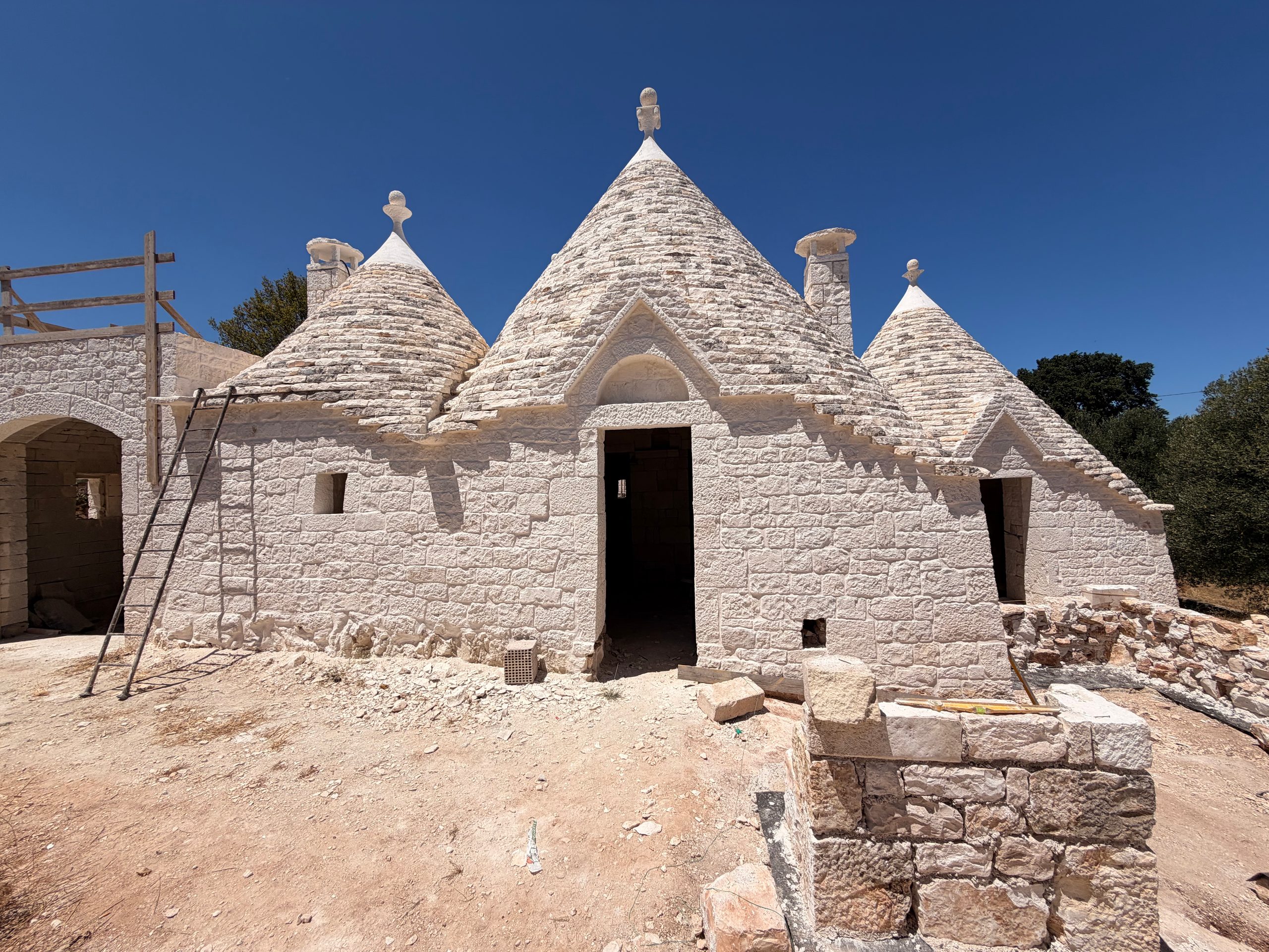 The restored trulli of Beyond Olives — four limestone cones and their pinnacles standing against a deep Puglian sky