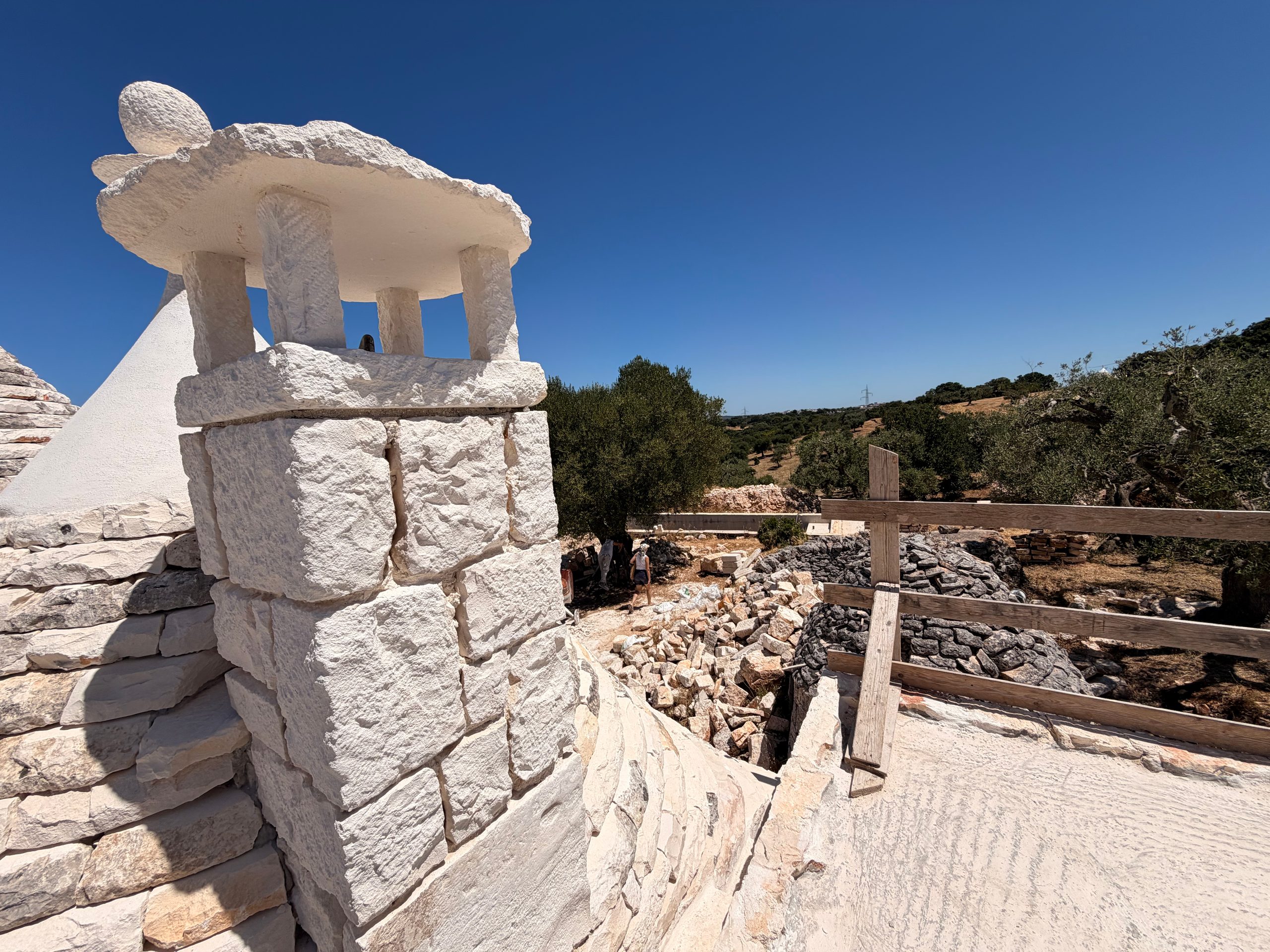 A newly built limestone chimney seen from the trullo roof, the olive grove falling away behind it