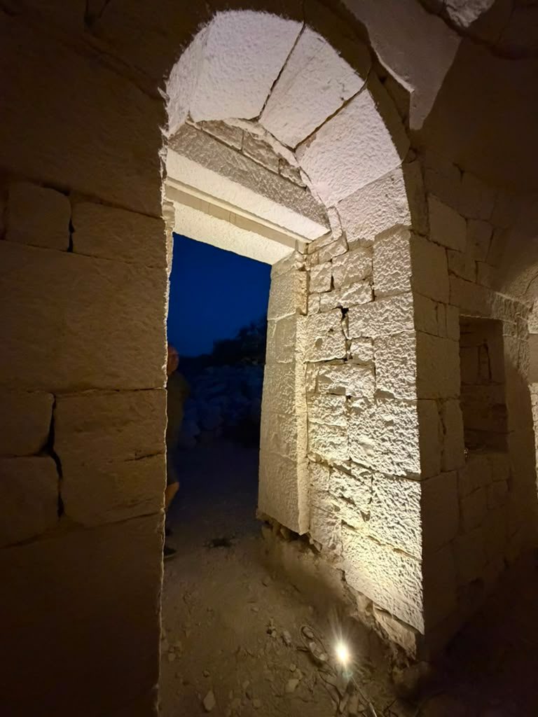 An arched stone doorway inside the trullo, opening onto the deep blue of a Puglian dusk