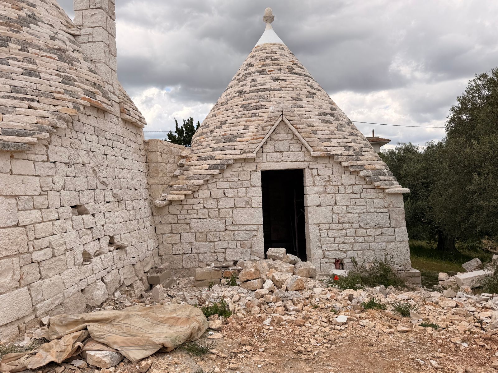 The trullo's conical limestone roof and arched stone doorway, mid-restoration