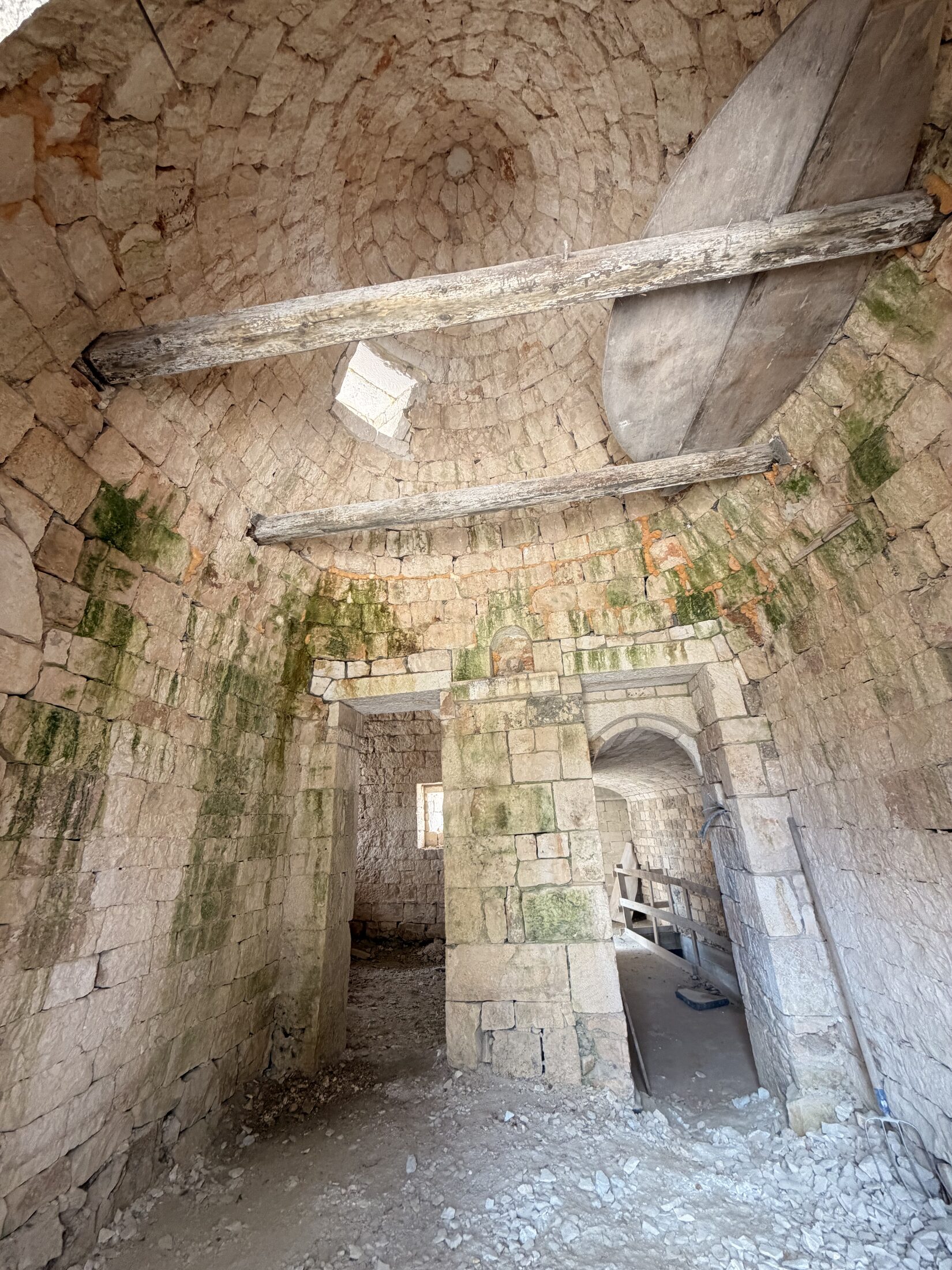 Inside the trullo, looking up at the dry-stone vault and timber beams above the bare stone floor
