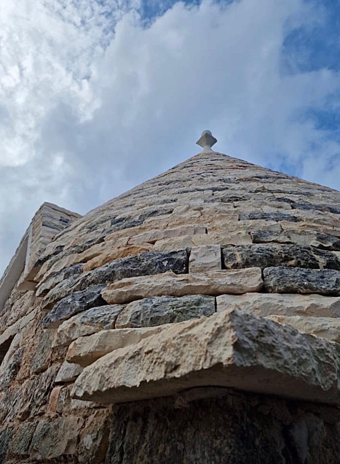 Dramatic upward view of the trullo dome rising against drifting Mediterranean clouds