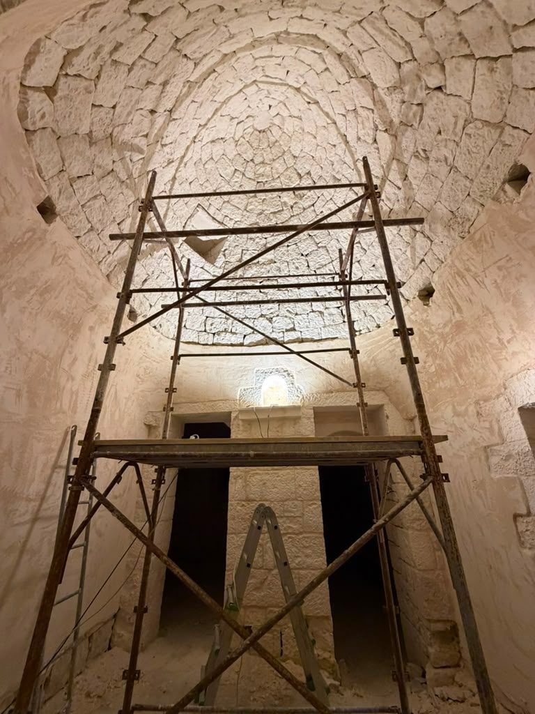Scaffolding standing inside a tall stone vault, the corbelled dome rising into shadow above it